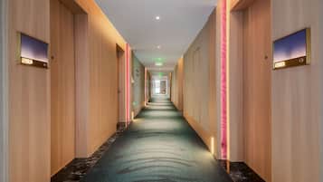 A hotel corridor with a carpeted floor, wooden walls, and illuminated door numbers.