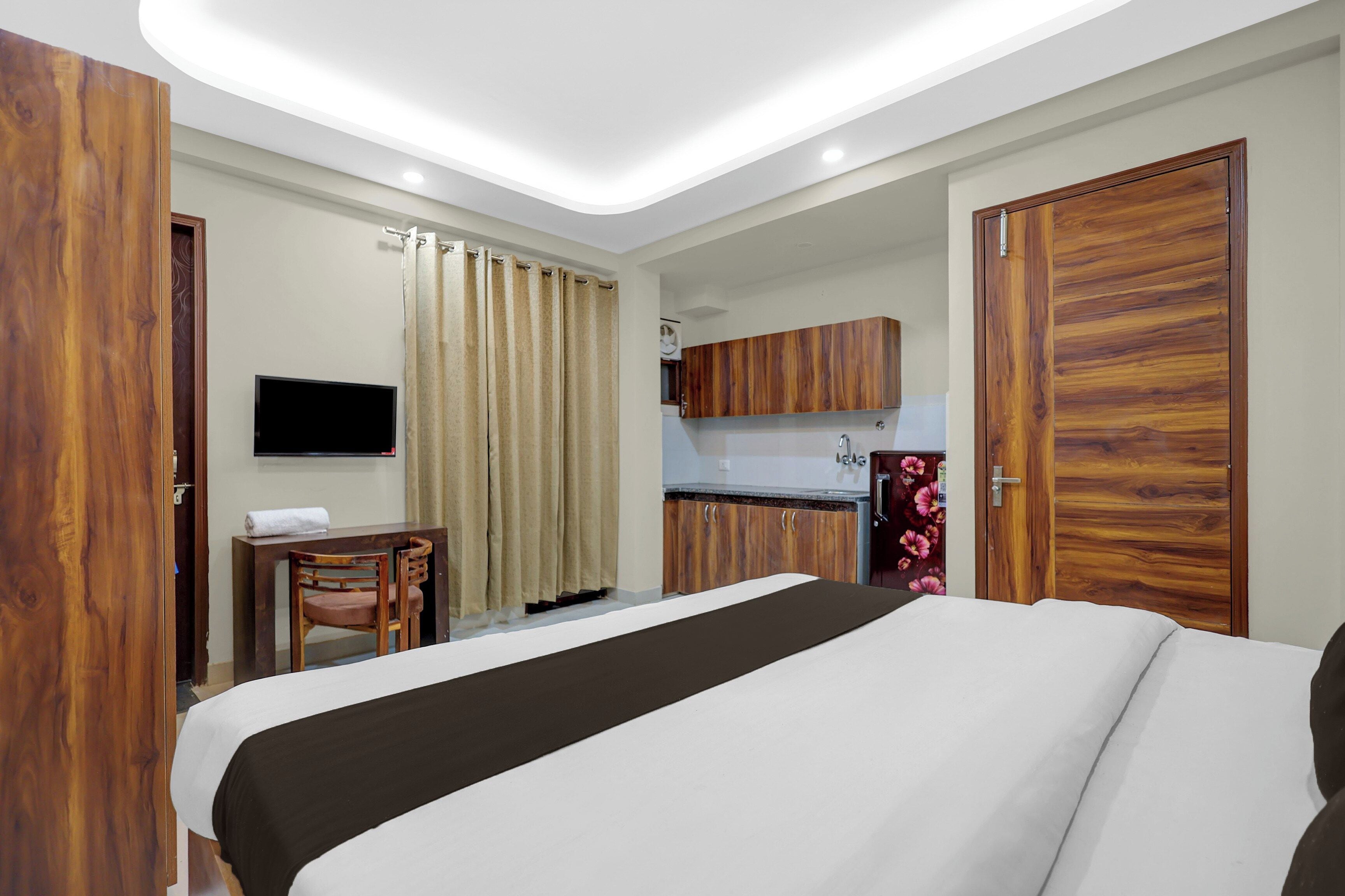 Una habitación de hotel con cama, escritorio, televisión y kitchenette.