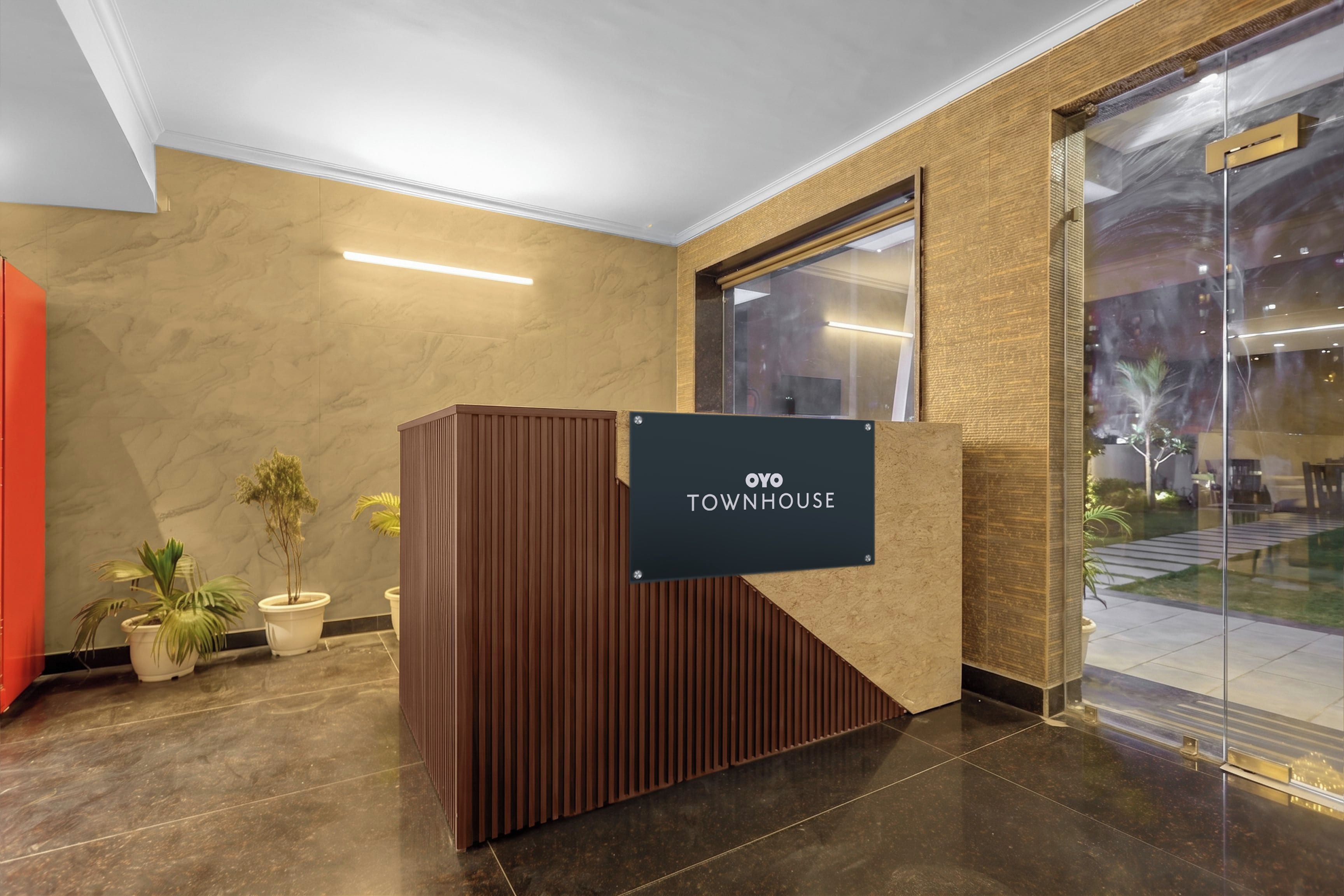 A reception area with a wooden reception desk, a sign reading 'OYO TOWNHOUSE', and a glass door leading to an outdoor area.