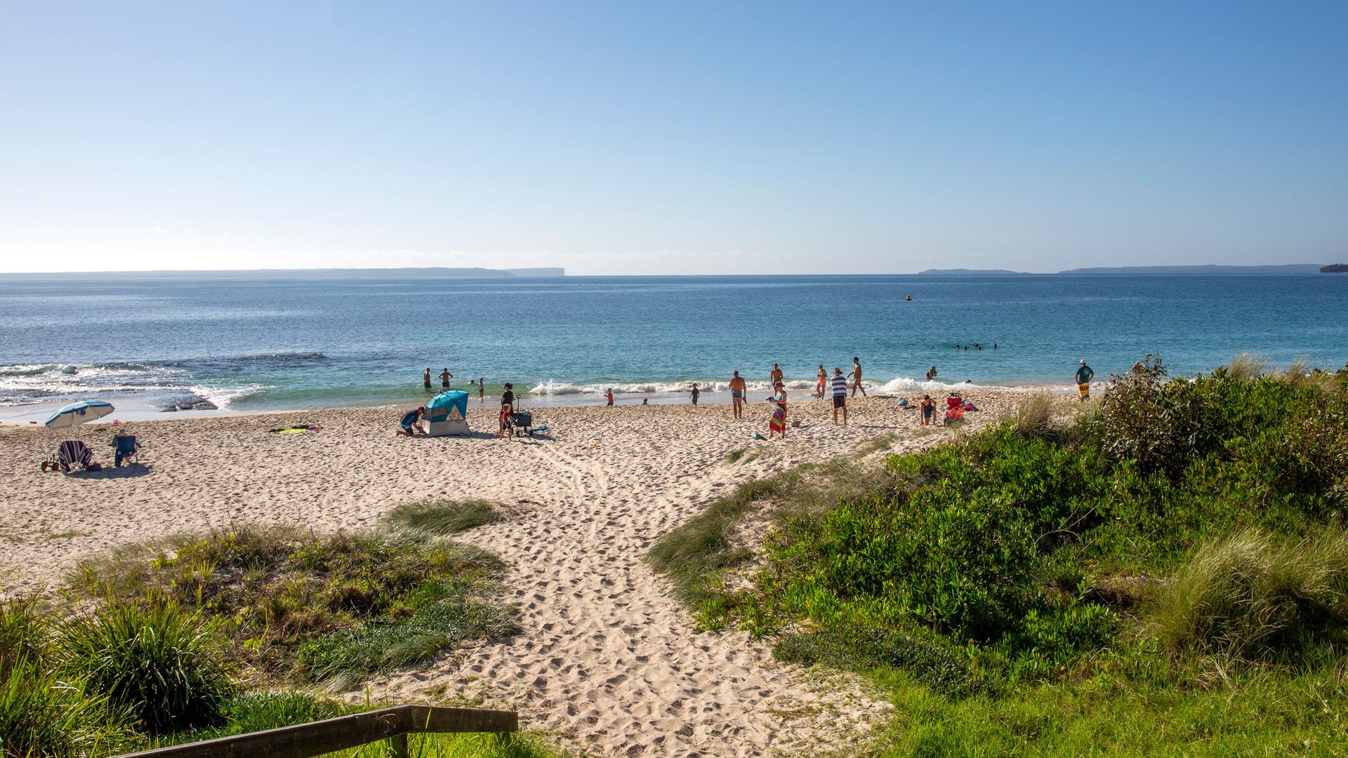 Une plage de sable fin, un ciel dégagé, une tente et des gens qui profitent de la mer.