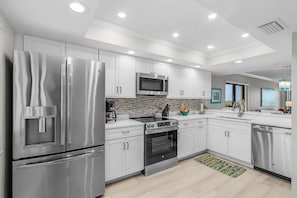 A modern kitchen with stainless steel appliances, white cabinetry, and a tiled backsplash. - Beachfront Bliss with Coastal Charm & Island Views - Condo Islands End 601 - Roelens (Fort Myers Beach)