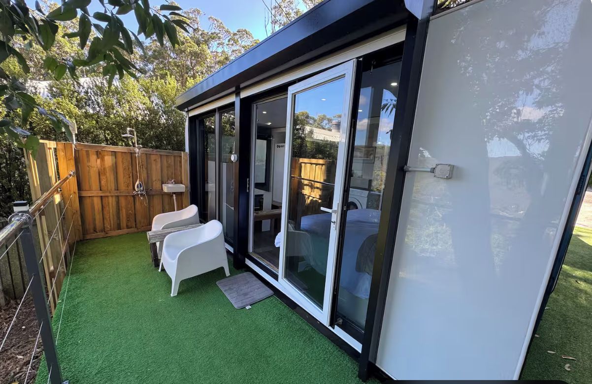 Un patio exterior moderno con cerca de madera, sillas blancas y puerta de cristal que da a una habitación.