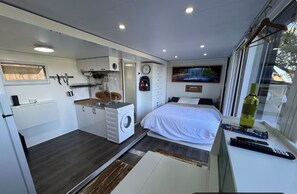 Ein kleines Schlafzimmer mit Bett, Fenster und einer Kochnische.