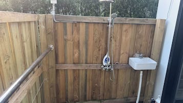 Un espace clos délimité par une clôture en bois, comprenant une douche, un lavabo et une main courante.