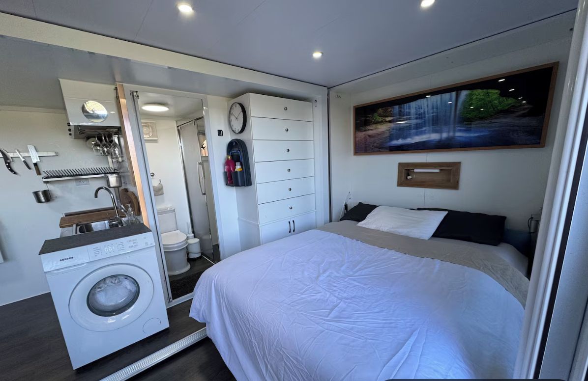 A modern bedroom with a bed, a washing machine, a dresser, and a large window.