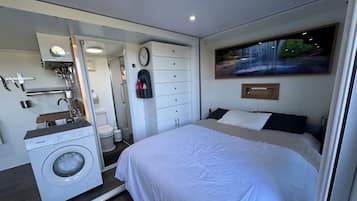A modern bedroom with a bed, a washing machine, a dresser, and a large window.