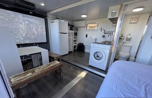 Un espacio habitable compacto con kitchenette, lavadora, banco y cama.