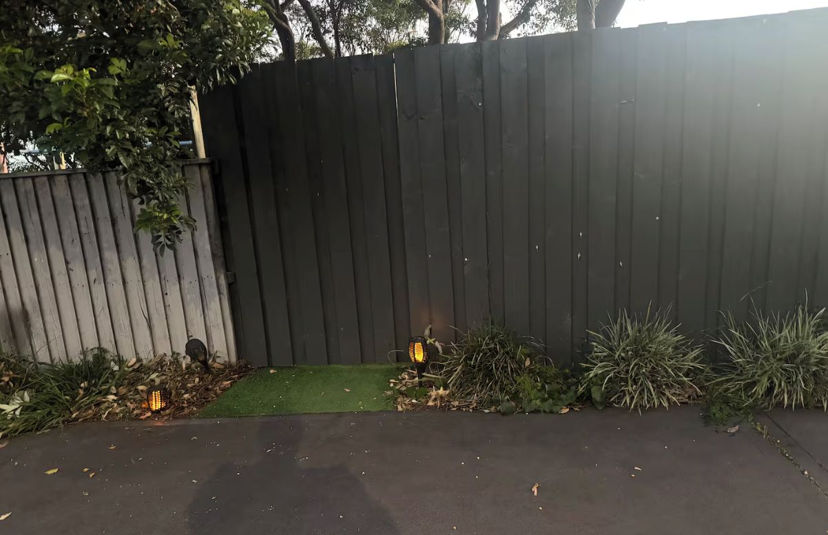 Une clôture en bois, avec une petite portion d’herbe et quelques plantes devant.