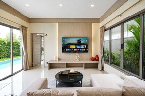 A modern living room with a flat-screen TV mounted on the wall, a glass coffee table, and a sofa. - Stylish 2 Bedrooms Villa with Pool & Tropical Garden (Tambon Rawai)