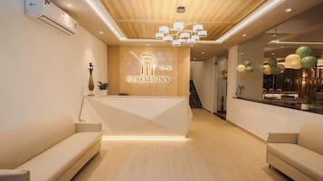 A reception area with a modern design, featuring a reception desk, sofas, a wooden ceiling, and a chandelier.