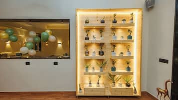 A room with a wooden floor, a wall-mounted shelf unit with potted plants, and a window with balloons.
