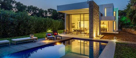 A modern house with a swimming pool, outdoor seating, and a stone pillar.