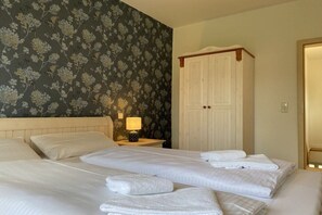 A hotel room with two beds, a nightstand with a lamp, a wardrobe, and a floral wallpaper. - Holiday home in Stiege with barbecue (Stiege)