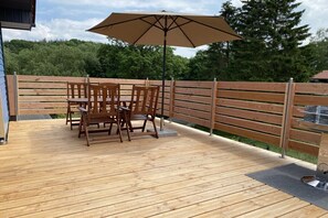 Une terrasse en bois avec une table et des chaises, un parasol et un barbecue en métal.