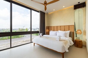 A modern bedroom with a large bed, a ceiling fan, and a view of the city. - 2BR Batu Bolong Luxury Smart Mediterranean Villa (Kuta Utara)