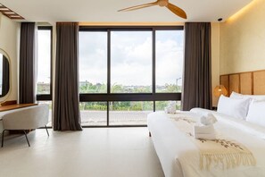 A hotel room with a large bed, a desk, and a view of the city through large windows. - 2BR Batu Bolong Luxury Smart Mediterranean Villa (Kuta Utara)