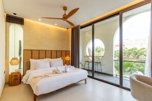 A modern bedroom with a bed, a ceiling fan, a large window, and a view of greenery outside. - 2BR Batu Bolong Luxury Smart Mediterranean Villa (Kuta Utara)