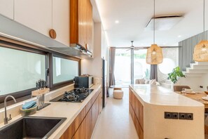 A modern kitchen with a central island, built-in appliances, and a view to the outdoor area. - 2BR Batu Bolong Luxury Smart Mediterranean Villa (Kuta Utara)