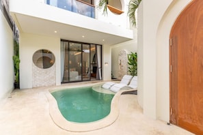 A modern outdoor pool area with a stone wall, a wooden door, and a glass entrance leading to a living space. - 2BR Batu Bolong Luxury Smart Mediterranean Villa (Kuta Utara)