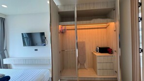 Ein kleines Hotelzimmer mit einem Bett, einem an der Wand befestigten Fernseher, einem integrierten Kleiderschrank mit einer Mikrowelle und einer Duschkabine.