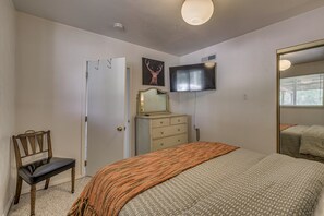A bedroom with a bed, a dresser, a chair, a television on the wall, and a door. - Walk to Midtown! Mountain-View Ruidoso Retreat (Ruidoso)