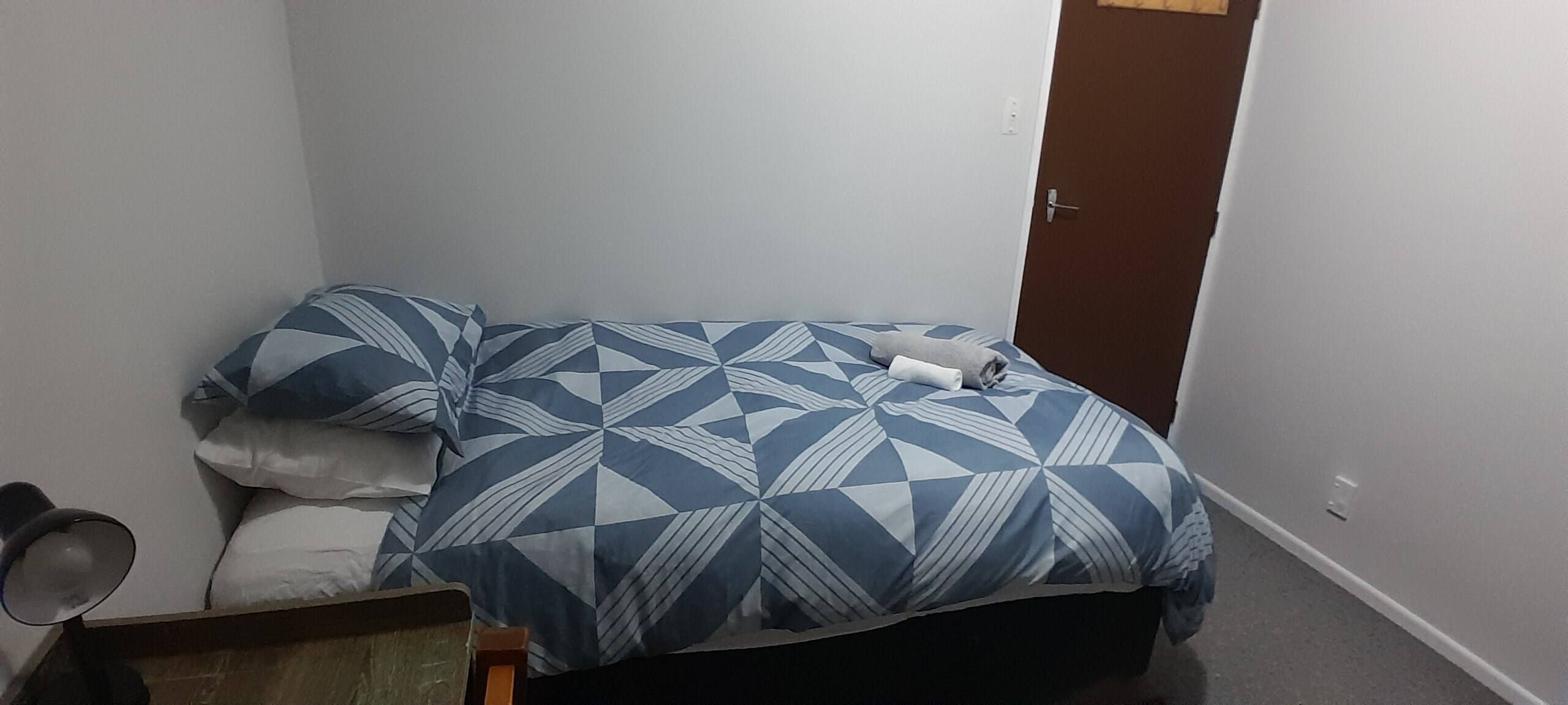 Et lille, aflangt rum med en seng, et natbord og en dør.