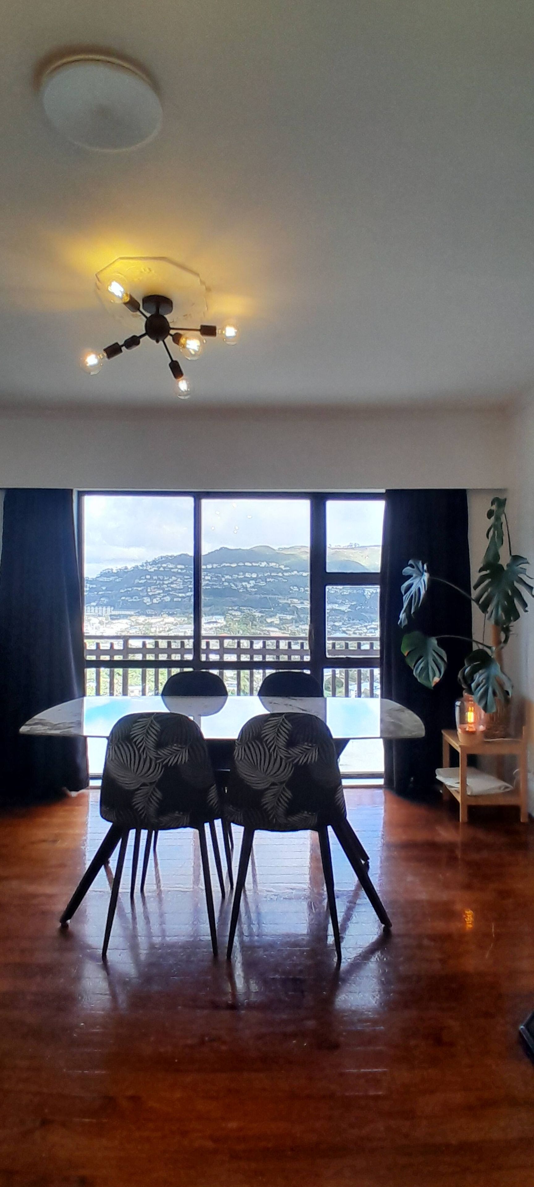 A room with a dining table and chairs, a ceiling fan, and a large window with a view of a cityscape.