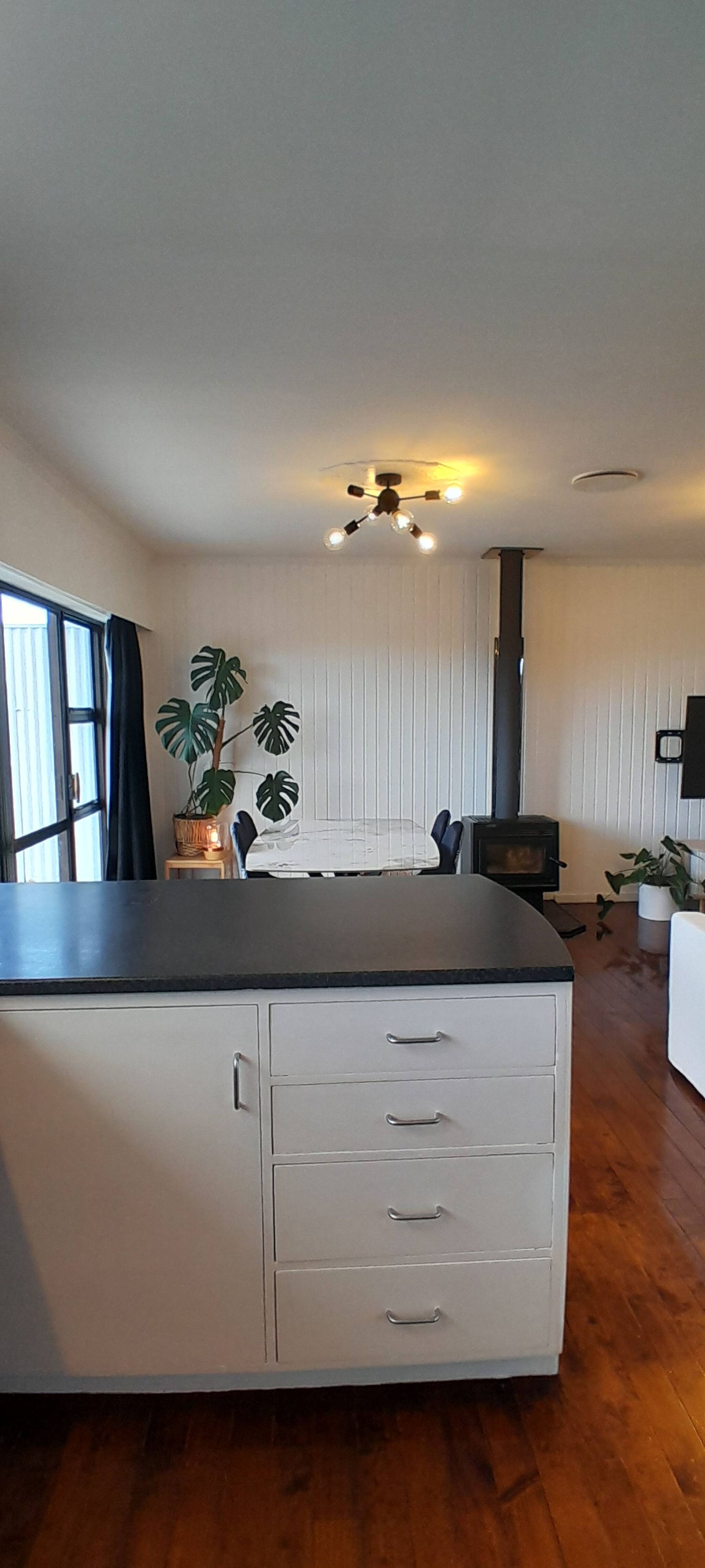 A spacious room with a large dining table, a built-in cabinet with drawers, a ceiling light fixture, and a window with curtains.