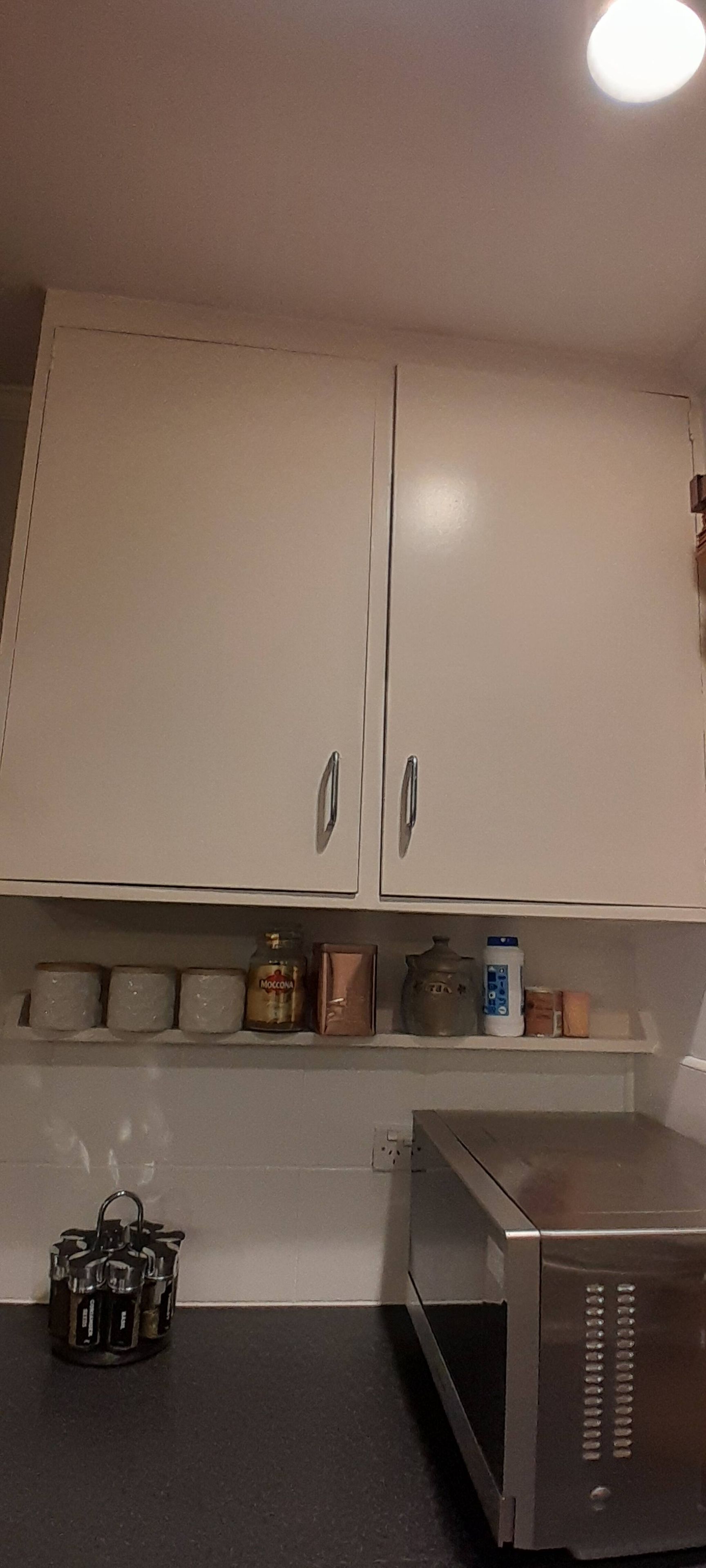 A kitchen with white cabinets, a microwave, and various kitchen items on the counter.