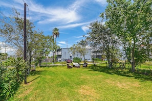 A residential area with a grassy lawn, a red car parked on the street, and a building with a balcony in the background. - New | Veteran Host | Luxe | Book Now for Wow (Galveston)