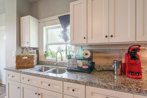 A kitchen with white cabinets, a granite countertop, a stainless steel sink, and a red coffee machine. - New | Veteran Host | Luxe | Book Now for Wow (Galveston)