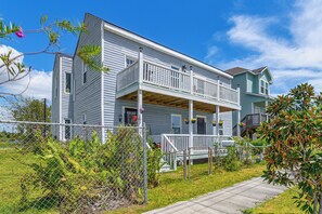 A two-story house with a porch, a fenced yard, and a clear sky. - New | Veteran Host | Luxe | Book Now for Wow (Galveston)