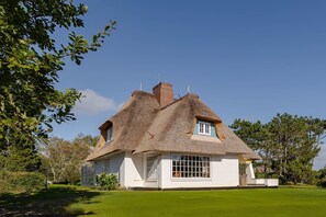 Ett traditionellt hus med halmtak och vit fasad, ett litet fönster och en välskött gräsmatta.