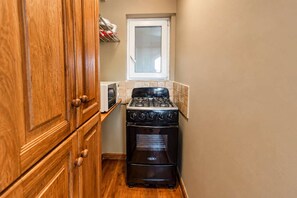A compact kitchen with wooden cabinets, a stove, and a window above the sink. - Central Sosua 1BR , Balcony , Hard Rock Perks (San Felipe de Puerto Plta)