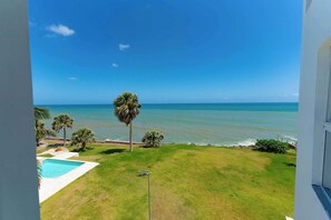A view of a pool, lawn, and ocean from a balcony.