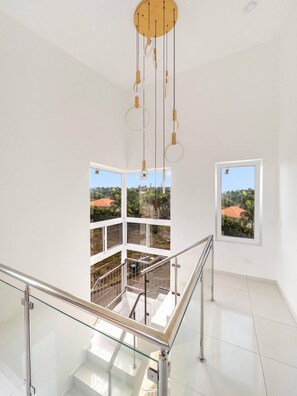 A modern interior with a glass staircase, a view of a residential area, and a wooden ceiling with hanging light fixtures. - Luxury BOSS Villa in Sosua Hispaniola (Sosúa)