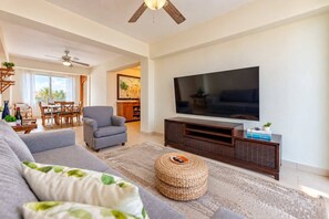 Ein modernes Wohnzimmer mit einem Flachbildfernseher, einem grauen Sofa, einer Holz-Unterhaltungsecke und einem Essbereich mit Tisch und Stühlen.
