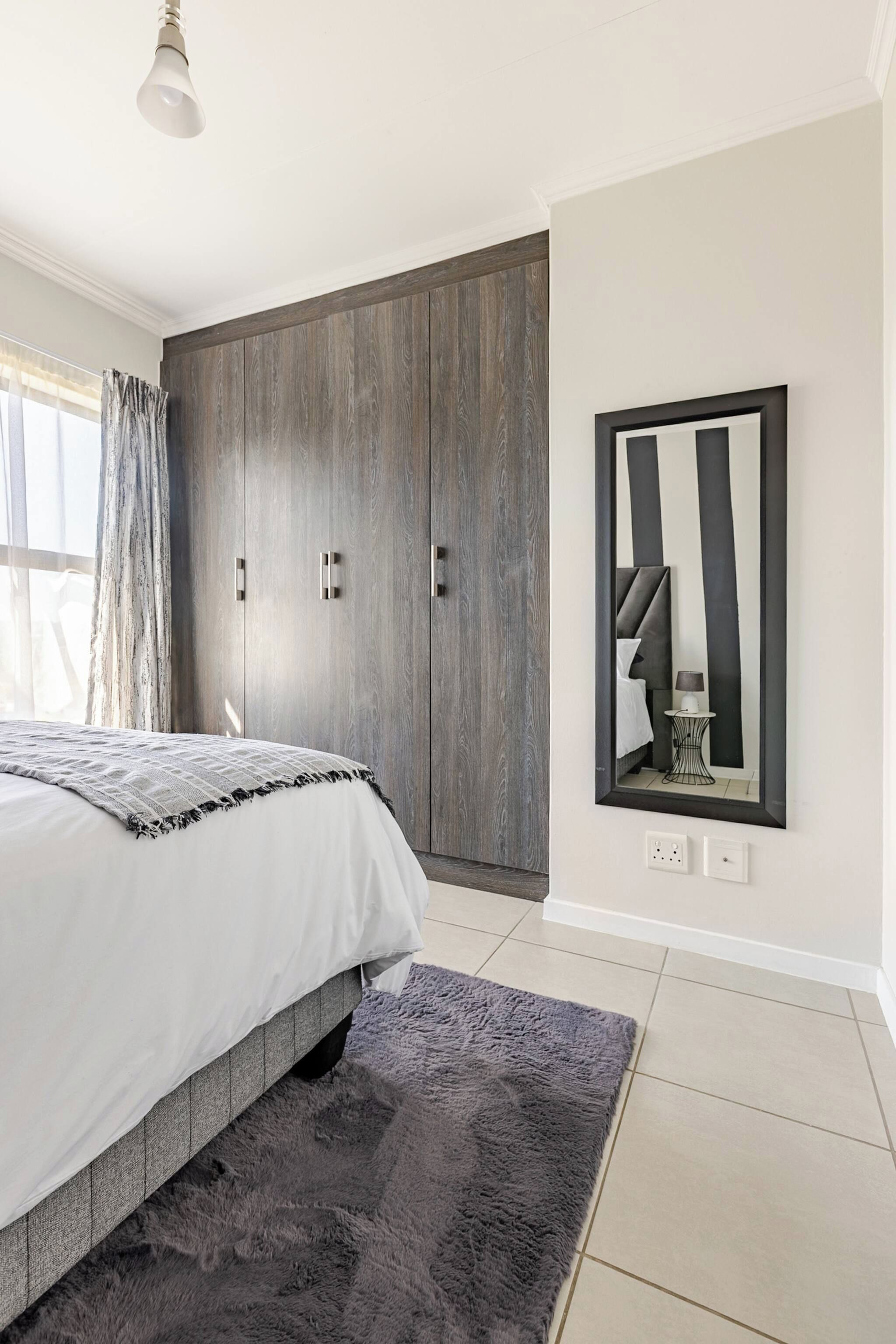 A bedroom with a bed, a wardrobe, a mirror, and a rug.