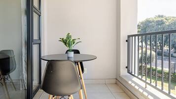 A balcony with a round table and two chairs, a potted plant, and a view of the street.