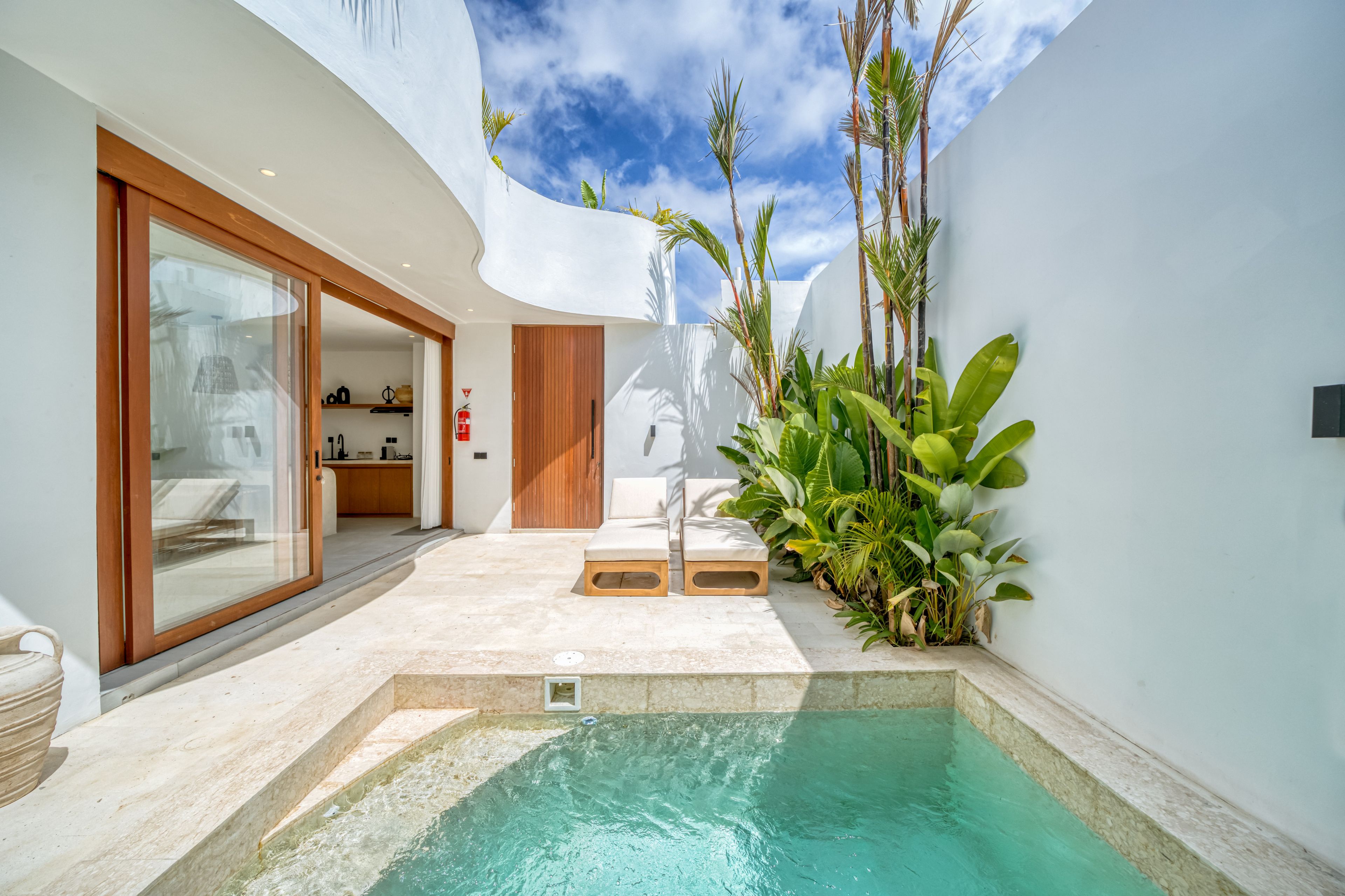 A modern outdoor pool area with a clear blue pool, a wooden deck, and tropical plants.