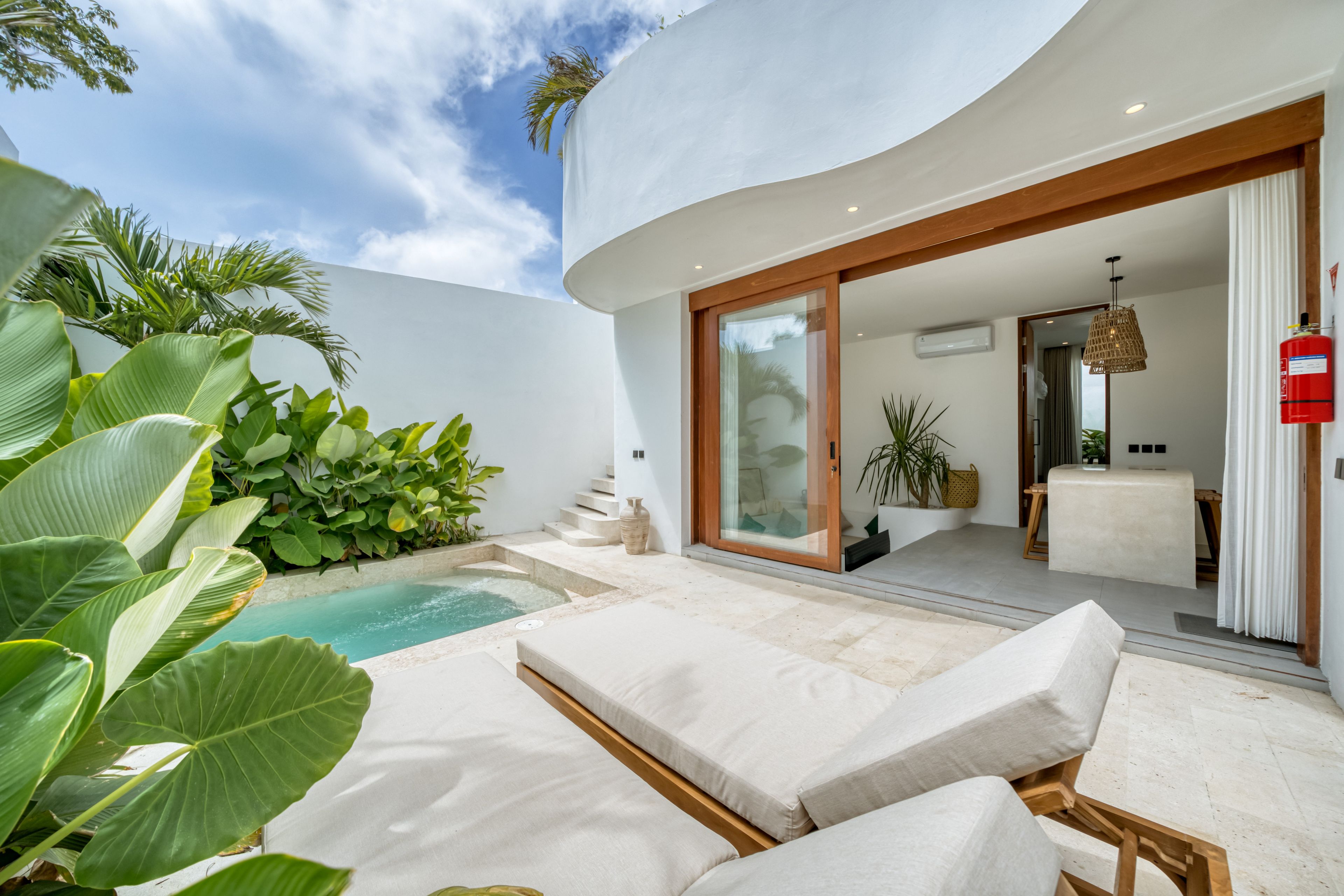 A modern outdoor pool area with lounge chairs, a hot tub, and lush greenery.