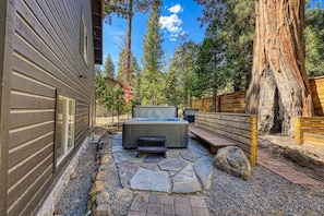 A hot tub in a stone-paved outdoor area with wooden benches and a large tree. - Silver Moon on the North Shore by Tahoe Getaways - Pet-Friendly 3BR w Hot Tub, Foosball & Horeshoes (Tahoe Vista)