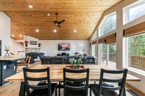 A spacious dining area with a wooden table and chairs, a ceiling fan, and a large window offering a view of the outdoors. - Silver Moon on the North Shore by Tahoe Getaways - Pet-Friendly 3BR w Hot Tub, Foosball & Horeshoes (Tahoe Vista)