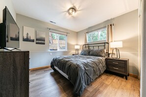 A bedroom with a bed, bedside tables, a TV, and artwork on the wall. - Silver Moon on the North Shore by Tahoe Getaways - Pet-Friendly 3BR w Hot Tub, Foosball & Horeshoes (Tahoe Vista)