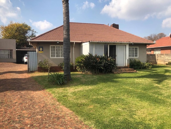 Einbungalow mit Ziegeldach, einer Haustür und einem kleinen Vorgarten mit Gras und einer Palme.