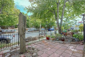 A paved outdoor area with a tree, potted plants, and a metal fence. - Staten Island Extended Stay w/ Suite & Patio (Staten Island)