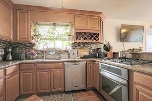 A kitchen with wooden cabinets, a dishwasher, an oven, and a wine rack. - Staten Island Extended Stay w/ Suite & Patio (Staten Island)