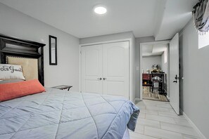 A bedroom with a bed, a nightstand, a mirror, and a door leading to a bathroom. - Staten Island Extended Stay w/ Suite & Patio (Staten Island)
