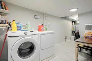 A laundry area with a Samsung washing machine, a dryer, and various cleaning supplies on a shelf. - Staten Island Extended Stay w/ Suite & Patio (Staten Island)