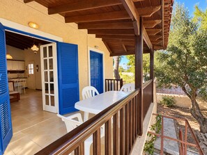 Un'area esterna coperta con ringhiera in legno, un tavolo bianco e persiane blu alle porte.